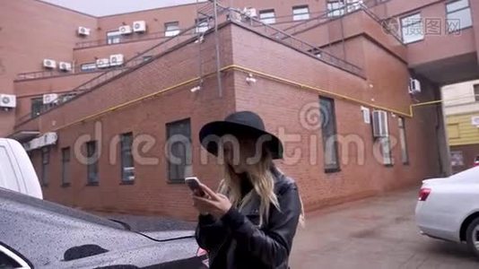 城市里的一个女孩在下雨时`用智能手机。 她很高兴视频