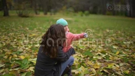 妈妈带着孩子在秋天公园。 快乐的年轻妈妈和小女孩在秋天的森林里休息。 慢动作视频