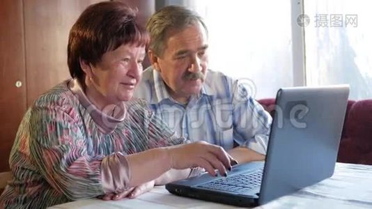 一对老夫妇坐在家里的笔记本电脑上。 女人看新闻，男人用手机说话视频