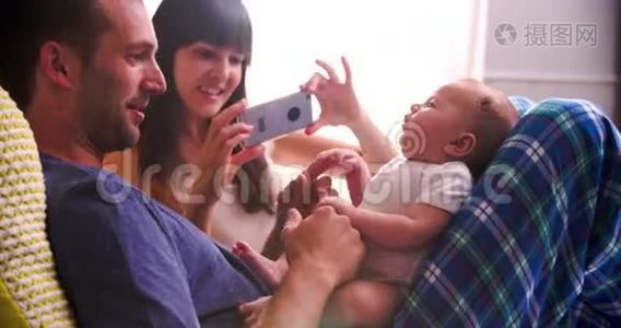 在床上为新生儿女儿拍照的父母视频