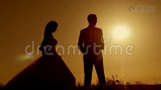 新娘和新郎的剪影在美丽的橙红色晚霞中亲吻视频