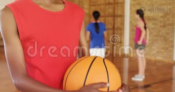 微笑的男孩拿着篮球，而球队在后台比赛视频