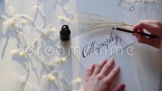 女艺术家的手写钢笔字体与书法字母在桌子上闪烁花环在工作室。视频