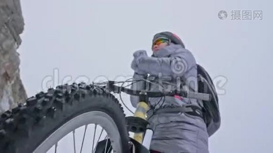 女人在冰上骑自行车。 女孩穿着银色羽绒服，自行车背包和头盔。 女人是视频