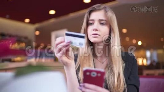 穿黑色夹克的金发女郎在咖啡馆A©。 她在智能手机上的银行卡数据方面处于领先地位。视频