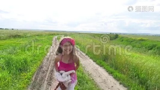 少女时代。 女孩带着一个娃娃少年在大自然的道路上奔跑在田野里。视频