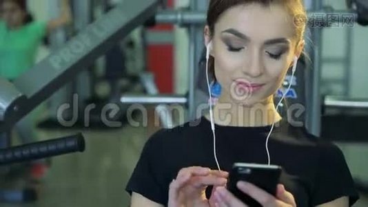 健身房里一个女孩带着手机和耳机的特写镜头视频