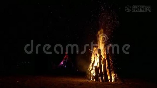 一个巨大的篝火在沙子和伟大的wigwam小屋的背景。 很多火花视频