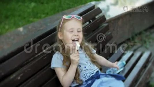 一个小女孩坐在城市的木凳上吃着冰淇淋，背景是一个城市公园视频