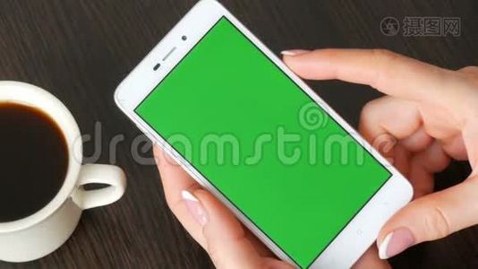漂亮的法国美甲女性手拿着一个白色智能手机，绿色屏幕靠近白色咖啡杯。 使用视频