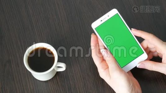 漂亮的法国美甲女性手拿着一个白色智能手机，绿色屏幕靠近白色咖啡杯。 使用视频