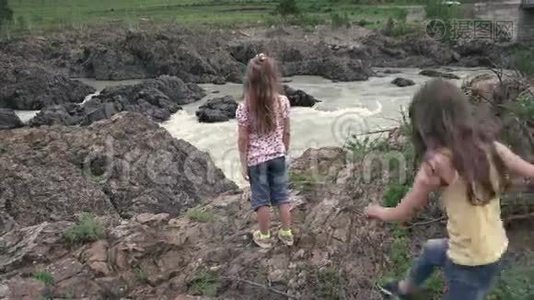 小女朋友在靠近一条山河的岩石上，欣赏令人叹为观止的景色。 女孩旅行者手牵手视频