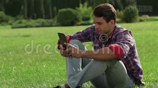 男性用平板电脑坐在草地上视频