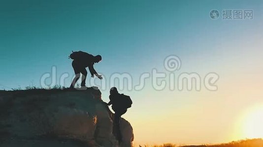 在两个登山者之间帮忙的剪影。 山顶上有两个徒步旅行者，一个人帮助一个人爬上一个纯粹的地方视频