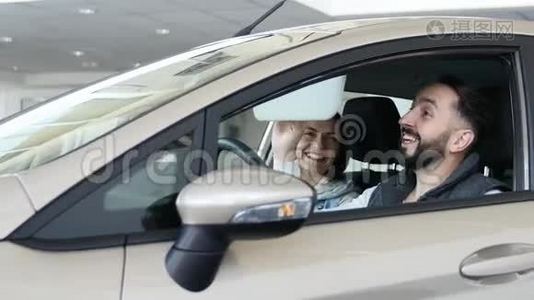 参观汽车经销商。 漂亮的一家人坐在他们的新车里，在说话和微笑。 年轻人用手指视频