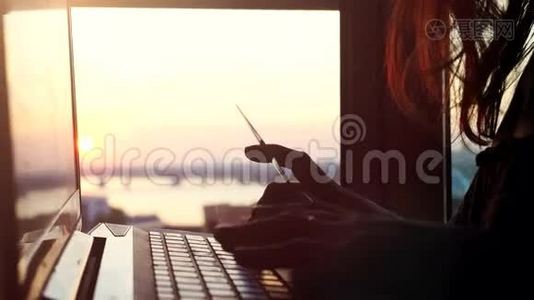 在美丽的日落时分，一位女士在城市背景模糊的背景下使用信用卡上网，并使用笔记本电脑视频