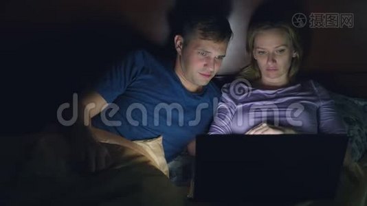 夫妻，男人和女人，在睡觉前在卧室的床上用笔记本电脑看电影。 看一部令人兴奋的电影，视频