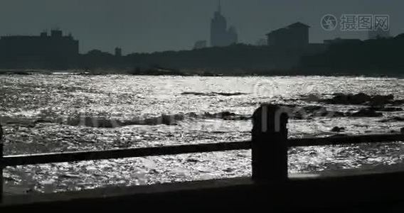 黄昏时分，人们沿着海岸漫步，海滨城市建筑和海洋波浪。视频