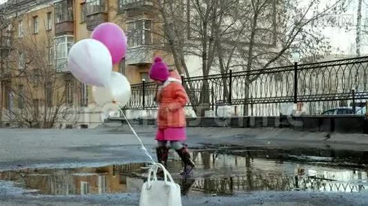 一个漂亮的小女孩在雨后的水坑上跳着五颜六色的气球视频