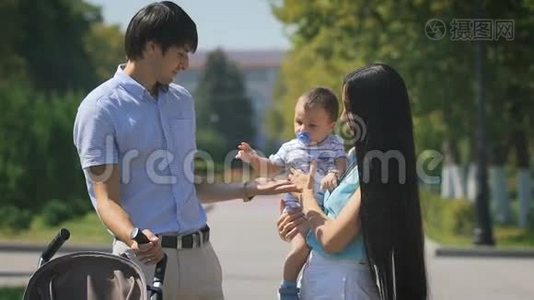年轻的一家人抱着一个小男孩走在城市公园里。视频