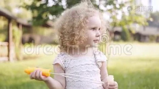 一个小女孩吹着肥皂泡，特写肖像美丽的卷发婴儿。视频