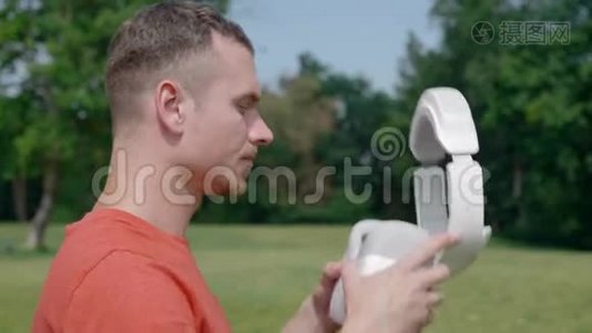 一个男人在公园里把一个VR耳机放在他的头上。视频