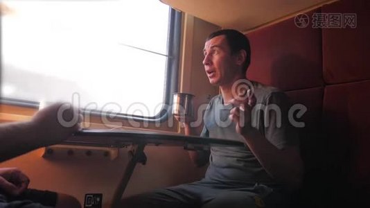 男人坐在火车车厢里，手里拿着铁路，喝着咖啡和茶。 慢动作视频。 两个人喝酒视频