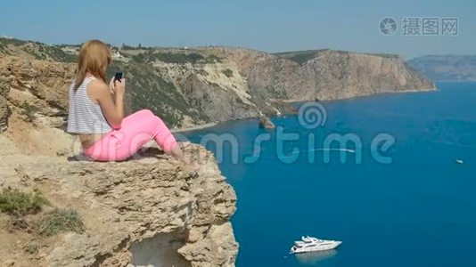 年轻女孩在坐在山上的蓝海附近拍照视频