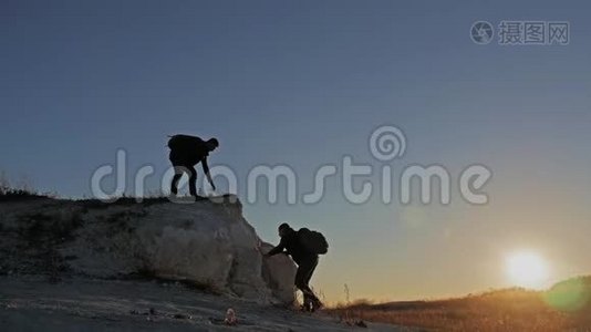 在两个登山者之间帮忙的剪影。 山顶上有两个徒步旅行者，一个人帮助一个人爬上一个纯粹的地方视频