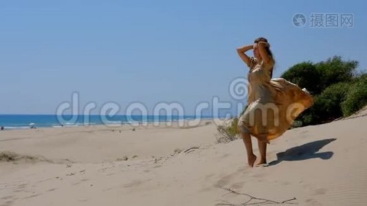 年轻漂亮的女人穿着金色的长裙站在靠近大海的沙丘上。视频