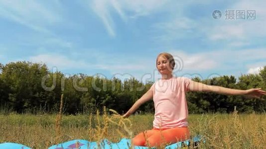 阳光明媚的夏日，一个可爱的成年女孩在公园户外做瑜伽视频