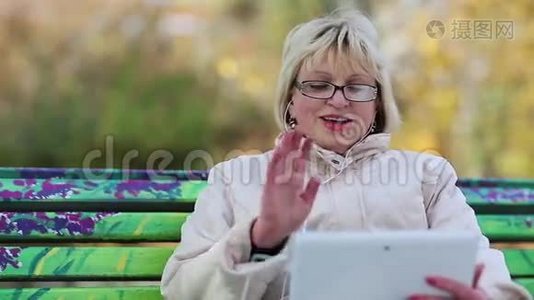 女人坐在长凳上，通过平板电脑交流视频