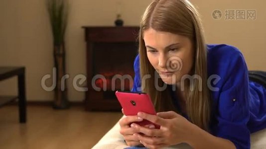 漂亮的年轻女人，一个智能手机躺在沙发上。 浏览互联网和微笑。视频