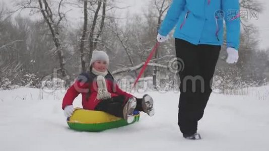 孩子和母亲在雪地里雪橇。 女儿和妈妈在圣诞节假期在冬季公园玩。 冬天视频