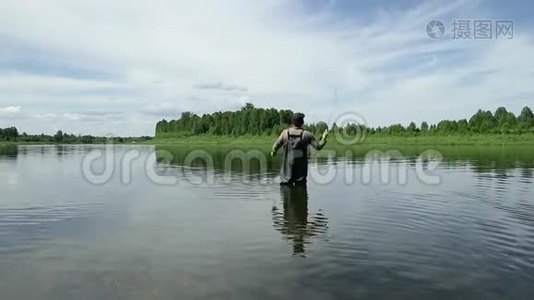 渔夫在一条平静的河里钓鱼。 一个穿着渔具的人在河里站着扔一根鱼竿视频