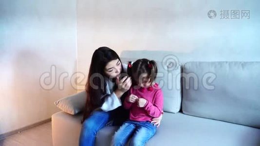 美丽的年轻母亲和小女儿坐在沙发上。视频