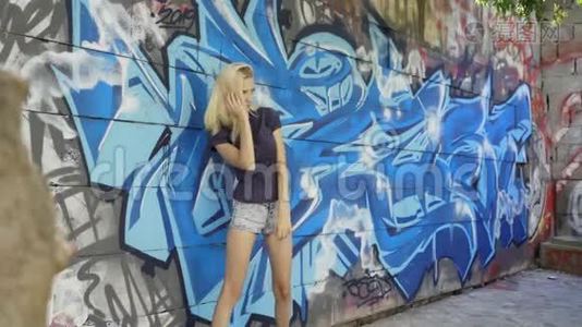 年轻的金发女孩在墙的背景上摆着涂鸦视频