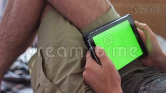 男人躺在家里的沙发上，看着有绿色屏幕的平板电脑视频