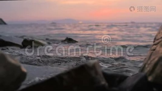 特写慢动作低角度小海浪在岩石海滩上翻滚.. 海边。 傍晚在卵石岩石海滩上日落视频