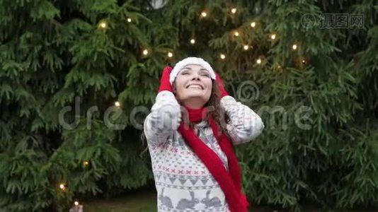 戴着红领巾和手套的圣诞老人帽子的快乐的女人，在圣诞树的背景下跳跃视频