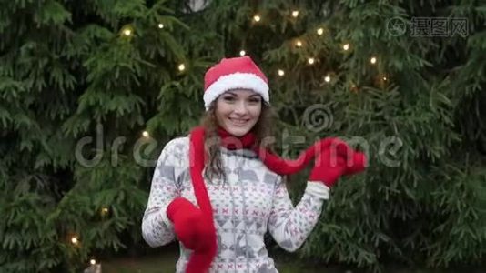 戴着红色围巾和手套的圣诞老人帽子的快乐的女人，在圣诞树的背景下跳跃视频