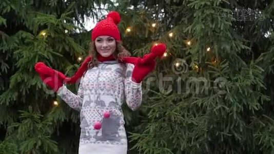 戴着红色围巾和手套的圣诞老人帽子的快乐的女人，在圣诞树的背景下跳跃视频