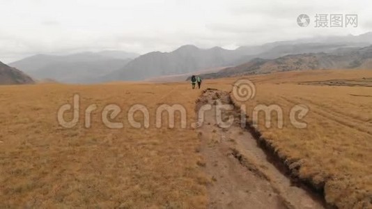 一对戴着帽子和太阳镜的大背包的旅行者男女在高山上漫步的鸟瞰图视频