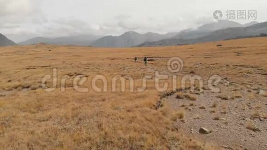 一对戴着帽子和太阳镜的大背包的旅行者男女在高山上漫步的鸟瞰图视频