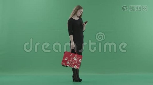 穿着小黑裙子的美女正在手机上发短信或上网，手里拿着她的购物视频