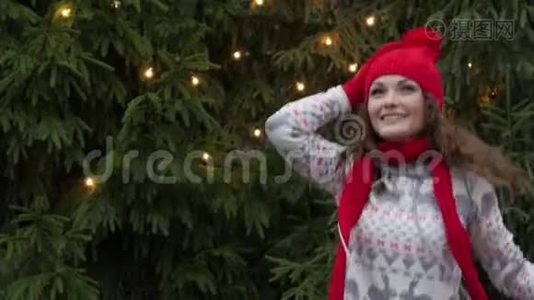 戴着红领巾和手套的圣诞老人帽子的快乐的女人，在圣诞树的背景下跳跃视频