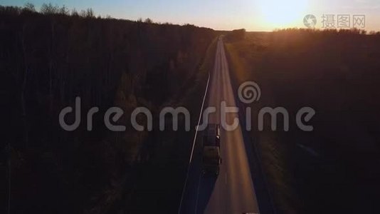 空中：带着集装箱的汽车在通往日落的道路上行驶。 卡车在高速公路上行驶。视频