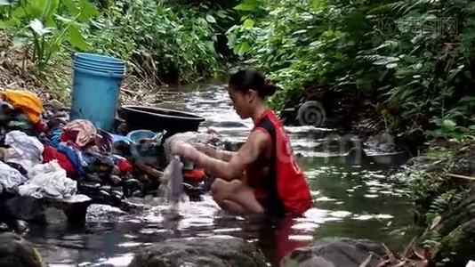 这个女人浸在膝盖的深水里，甚至在污染的河流里洗衣服。视频