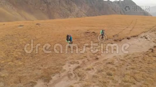 一对戴着帽子和太阳镜的大背包的旅行者男女在高山上漫步的鸟瞰图视频