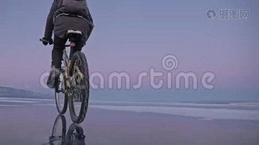 人在冰上骑自行车。 骑自行车的人穿着灰色的羽绒服，背包和头盔。 冰冻的冰视频